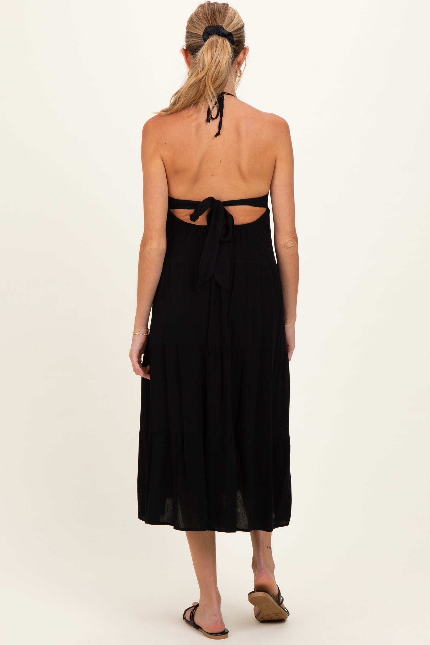 woman wearing a black halter neck maternity dress with a tie-back detail and flared skirt, showing a baby bump