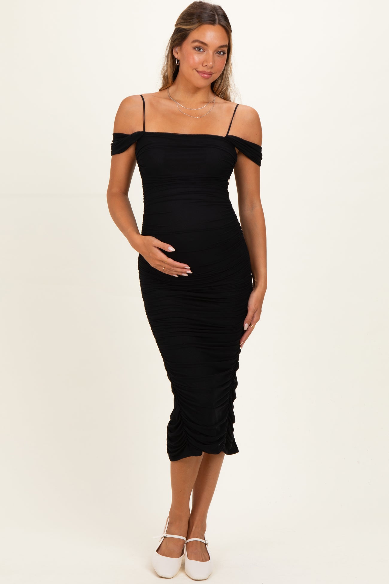woman wearing a black off-the-shoulder ruched maternity dress and holding her baby bump