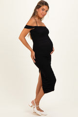 woman wearing a black off-shoulder maternity dress with ruching and a side slit, displaying her baby bump