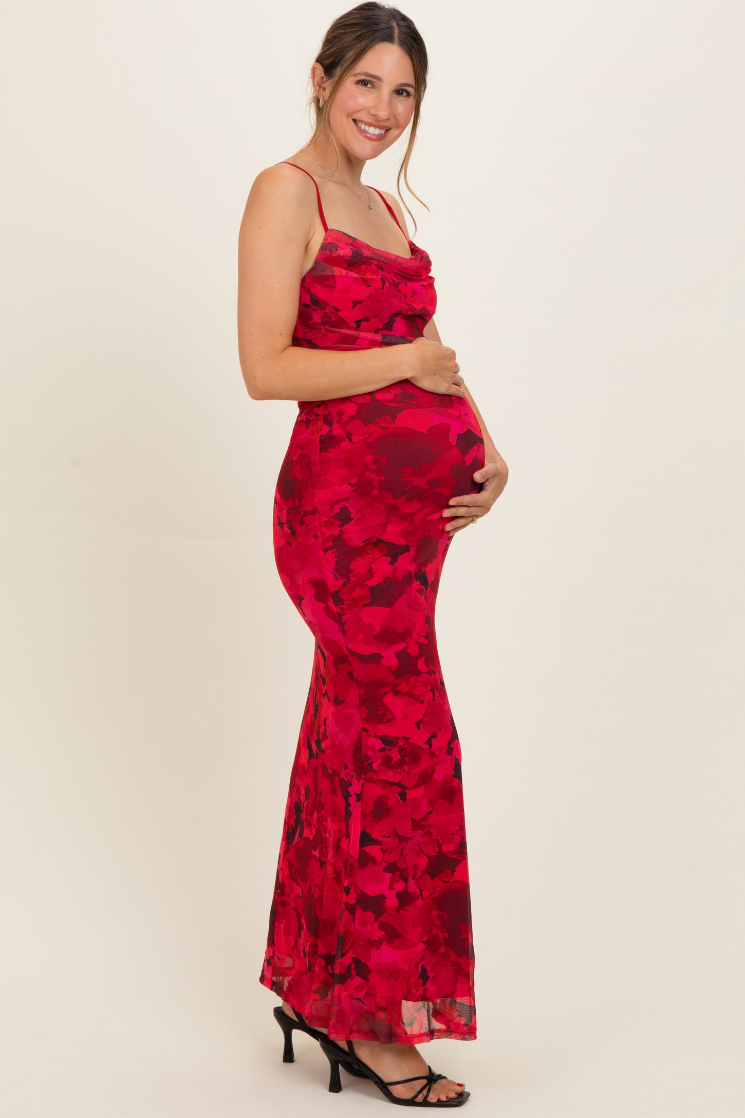woman wearing a red floral maternity gown with spaghetti straps and a fitted silhouette, holding her baby bump