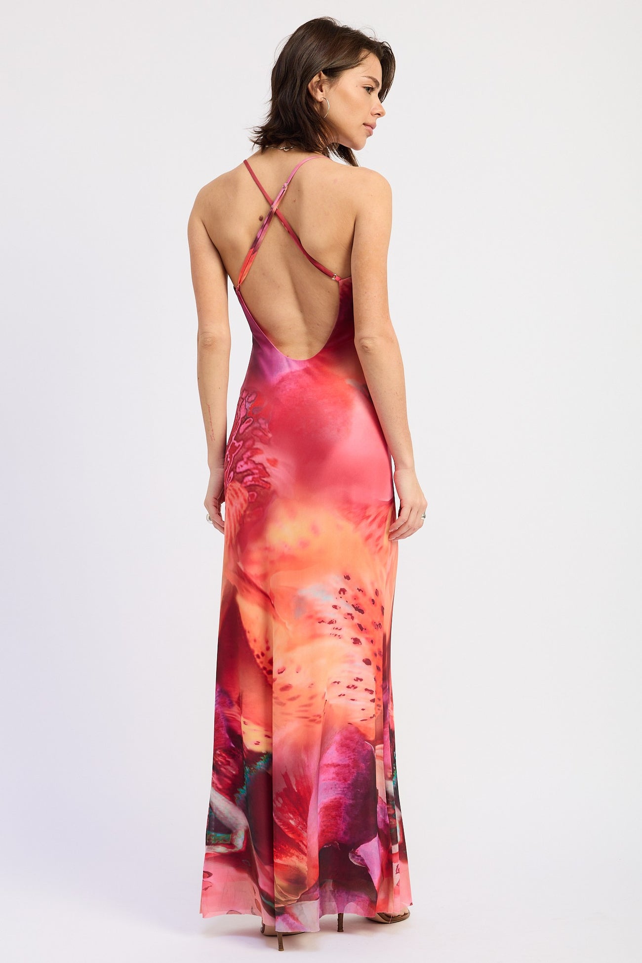 woman wearing a vibrant pink backless maxi dress with crisscross straps and a colorful abstract print