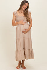 woman wearing a beige maternity maxi dress with ruffled straps and holding her baby bump