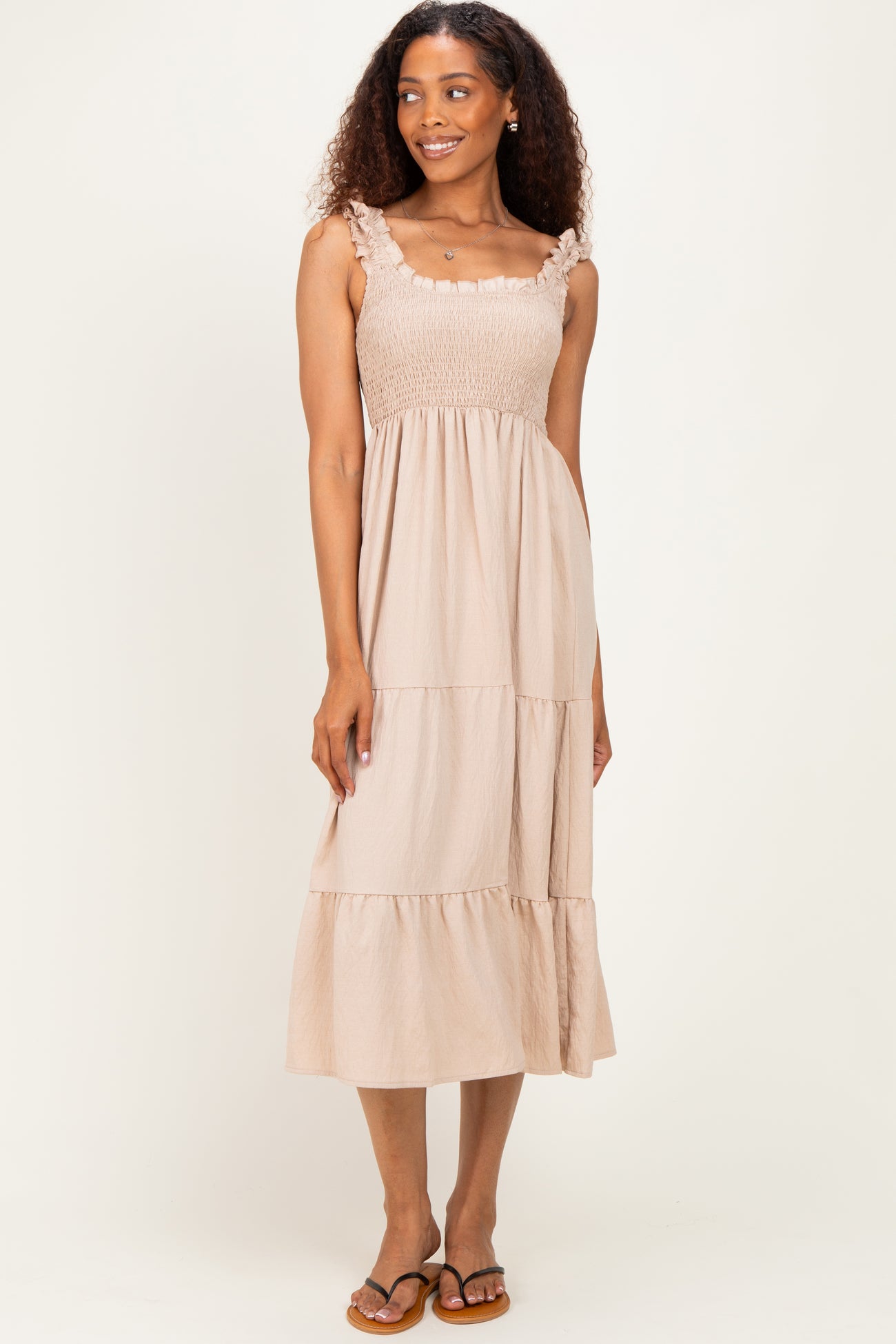 woman wearing a light beige smocked maxi dress with ruffle straps and a tiered skirt
