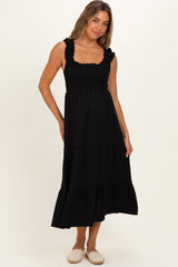 woman wearing a black maternity dress with smocked bodice and tiered skirt, featuring ruffle straps and a flowing style