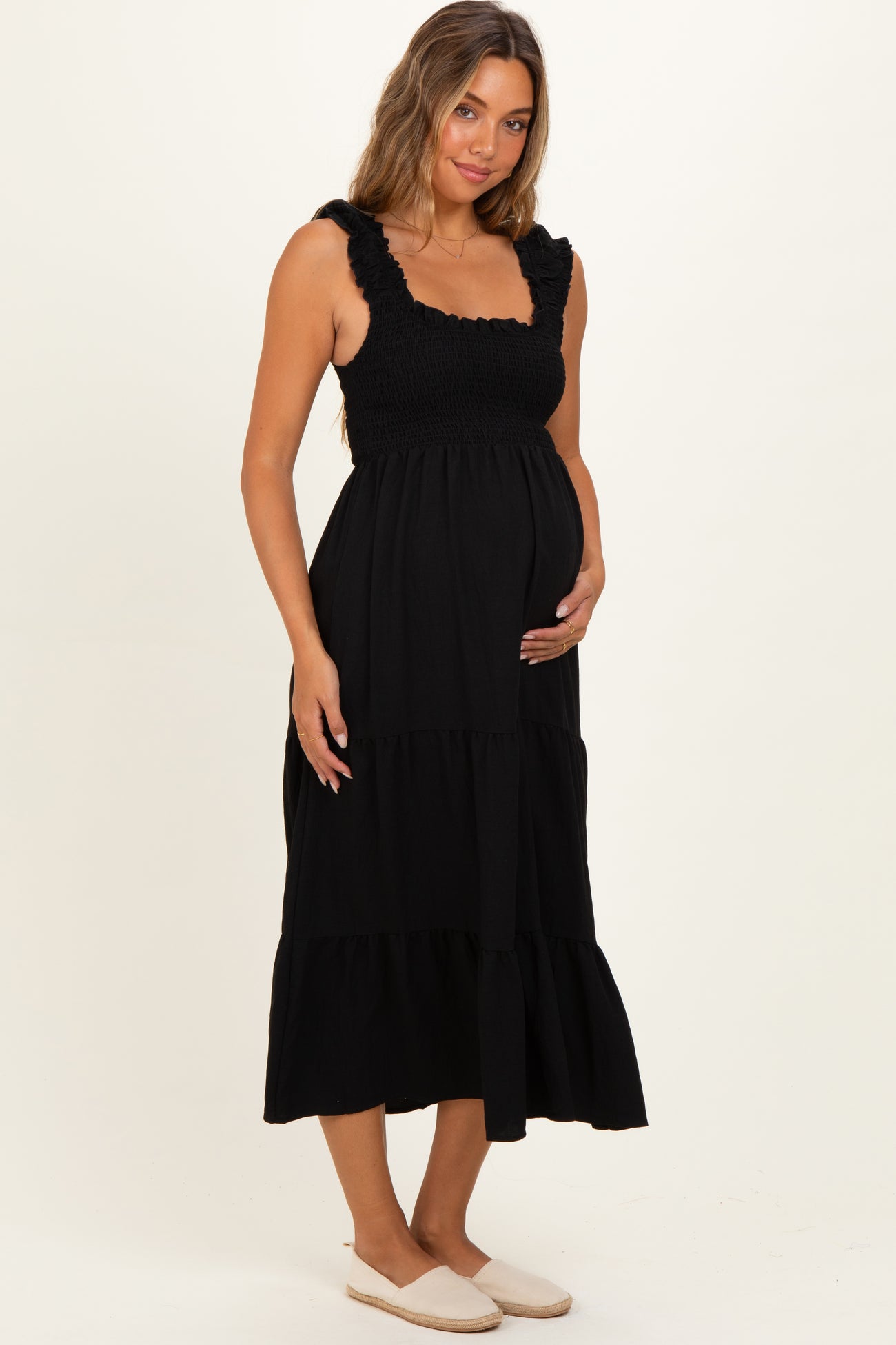 woman wearing a black maternity maxi dress with a smocked bodice and tiered skirt, holding her baby bump
