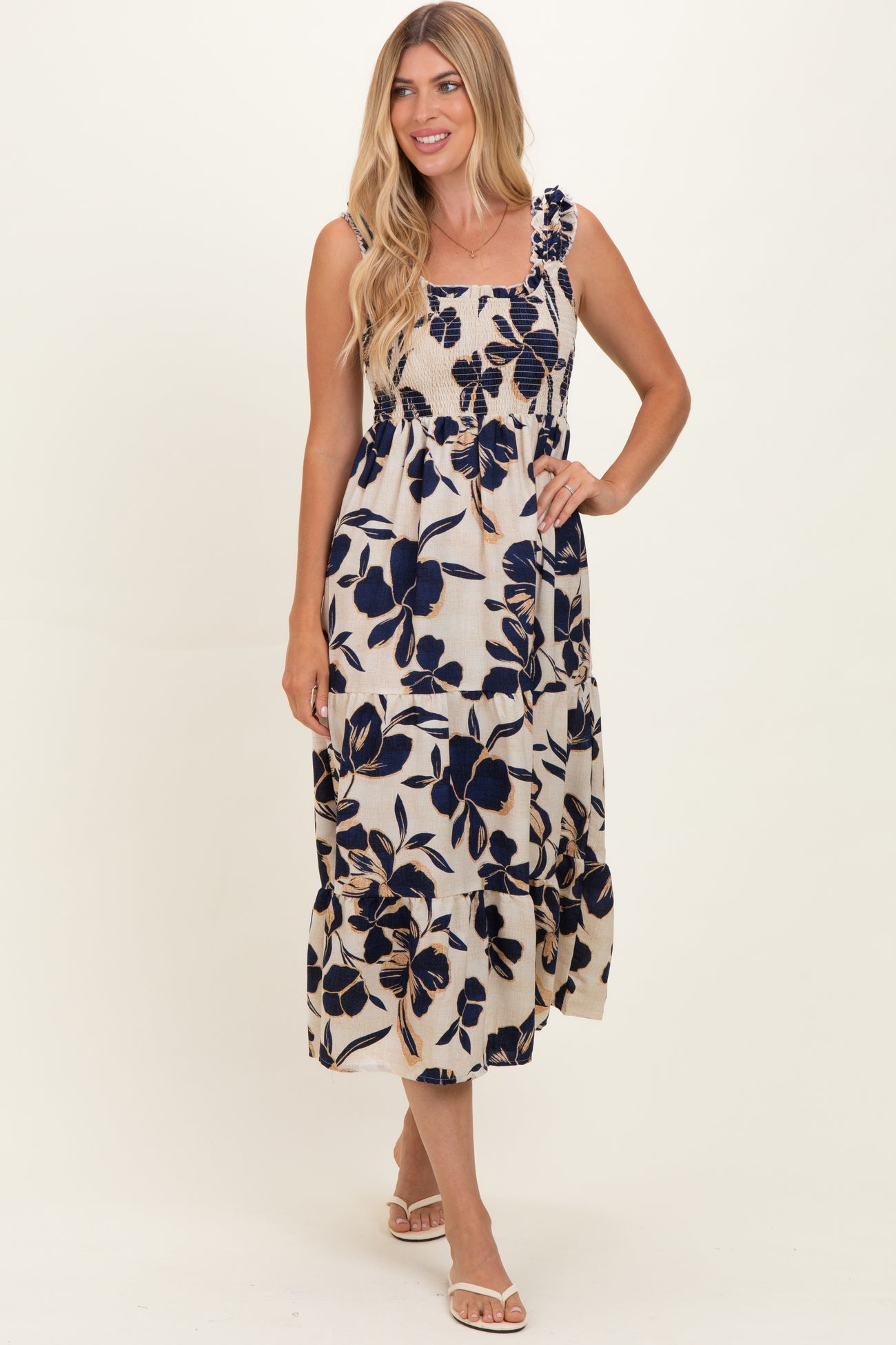 woman wearing a floral print maxi dress with navy blue flowers on a cream background and ruffled straps
