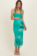 woman wearing a teal floral maternity dress with a fitted silhouette and spaghetti straps, holding her baby bump