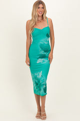 woman wearing a teal midi dress with floral print and spaghetti straps, smiling against a neutral background