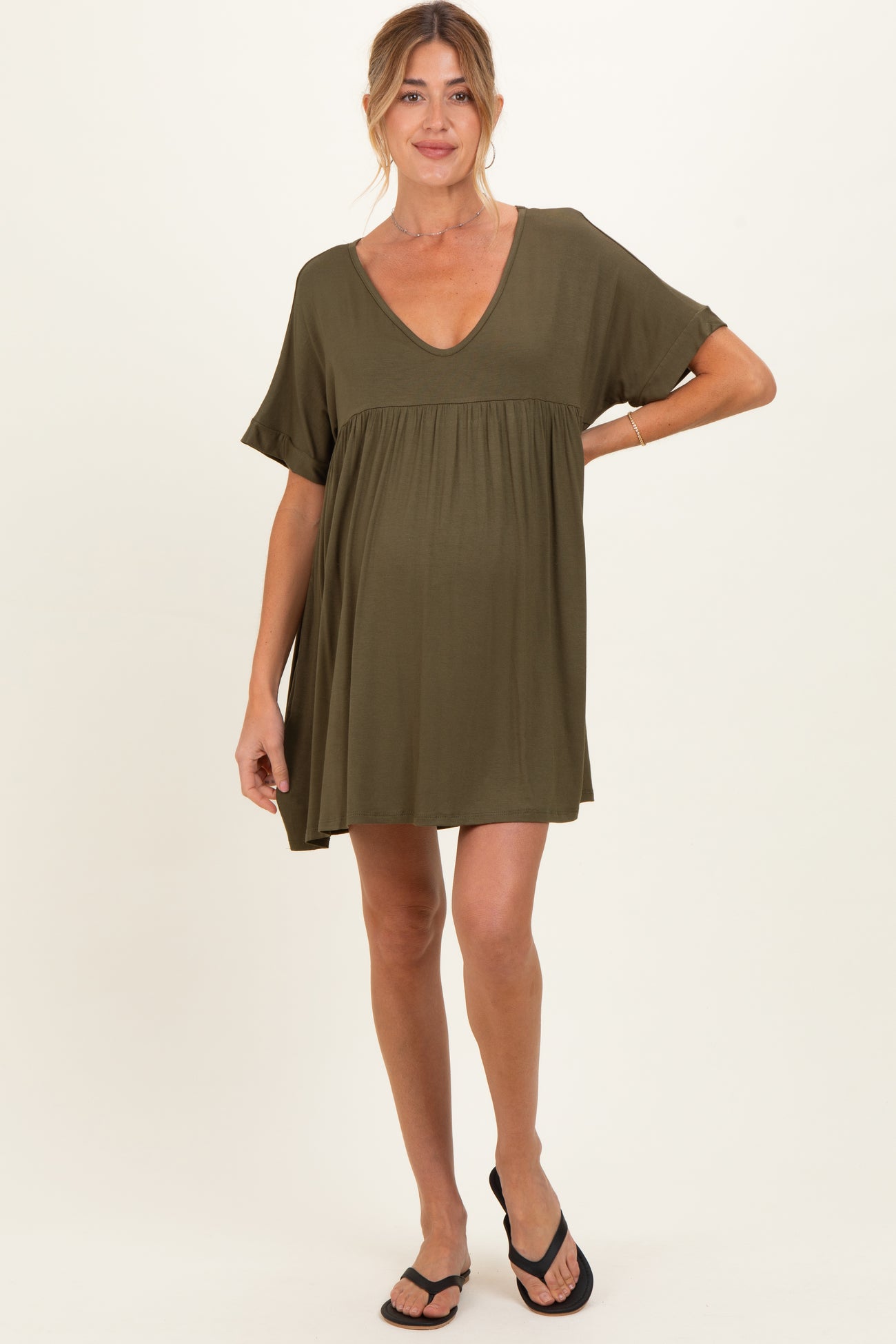 woman wearing an olive green maternity dress with short sleeves and a V-neck, slightly showing a baby bump