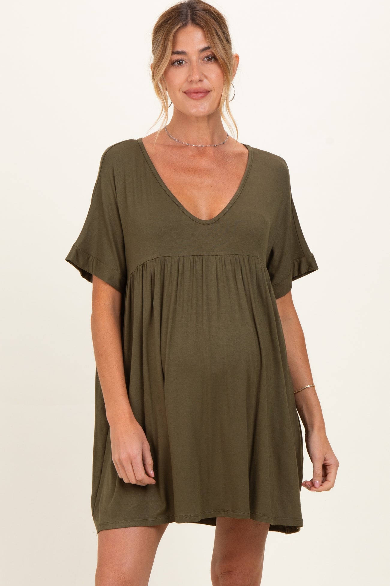 woman wearing an olive green maternity dress with a deep v-neck and short sleeves, showing her baby bump