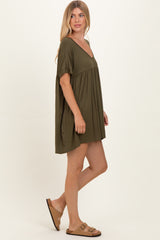 woman wearing an olive green short sleeve swing dress and brown sandals, posing sideways against a neutral background