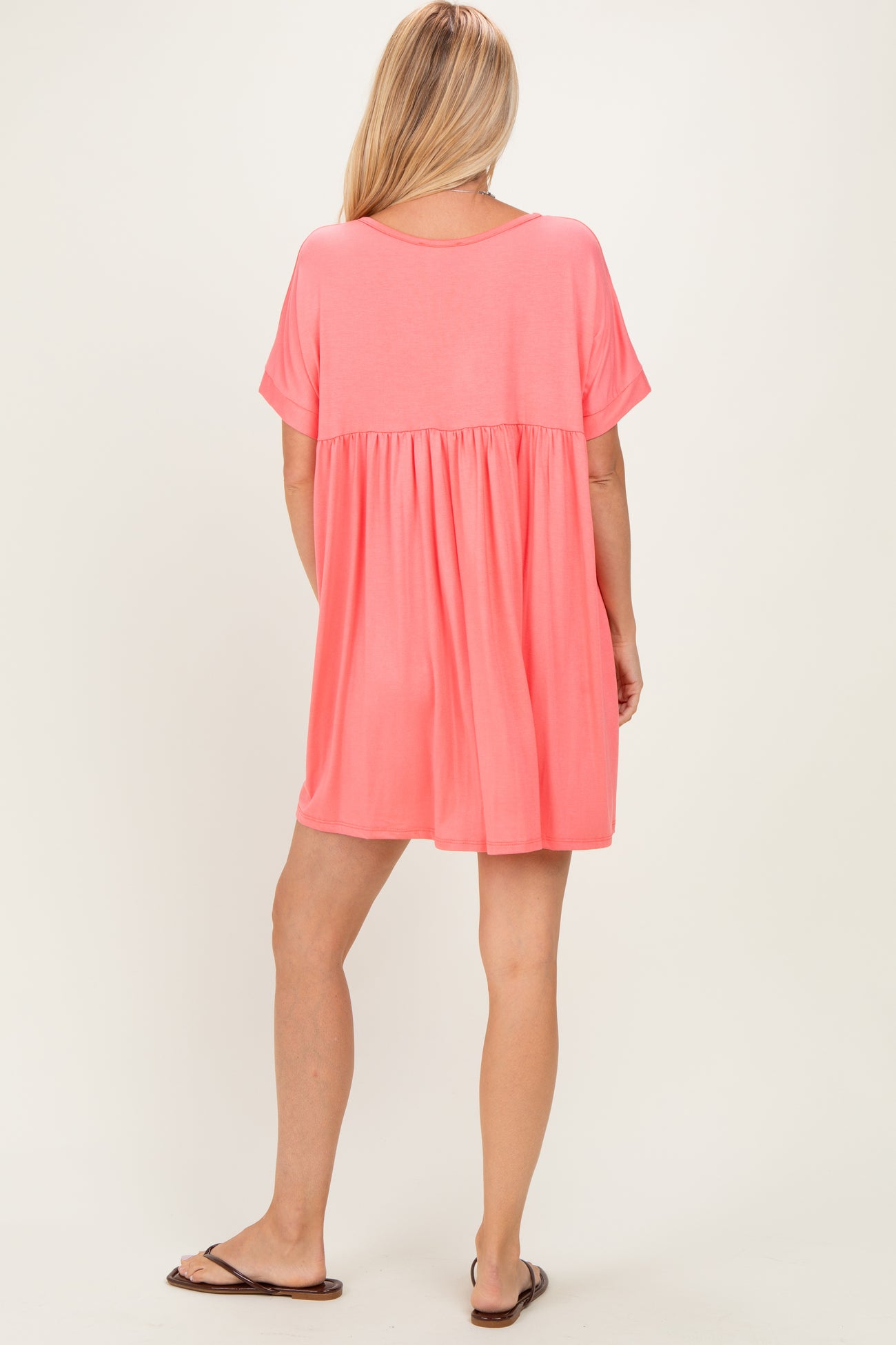 woman wearing a relaxed fit coral short sleeve dress with a tiered skirt and a scoop back