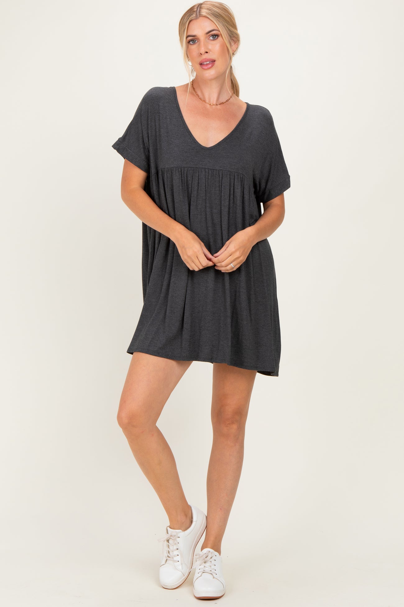woman wearing a dark gray short sleeve mini dress with a v-neck and relaxed fit, paired with white sneakers