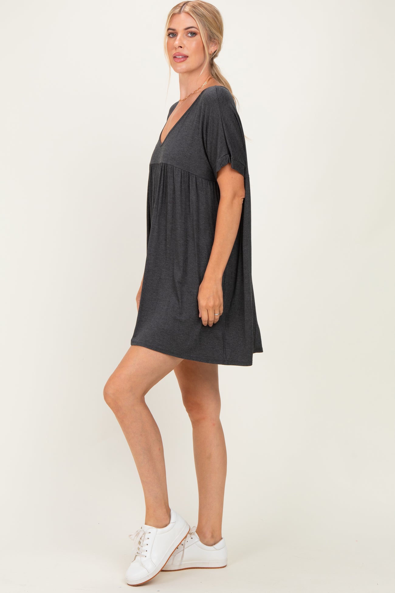 woman wearing a dark gray short sleeve v-neck dress with a flared hem and white sneakers