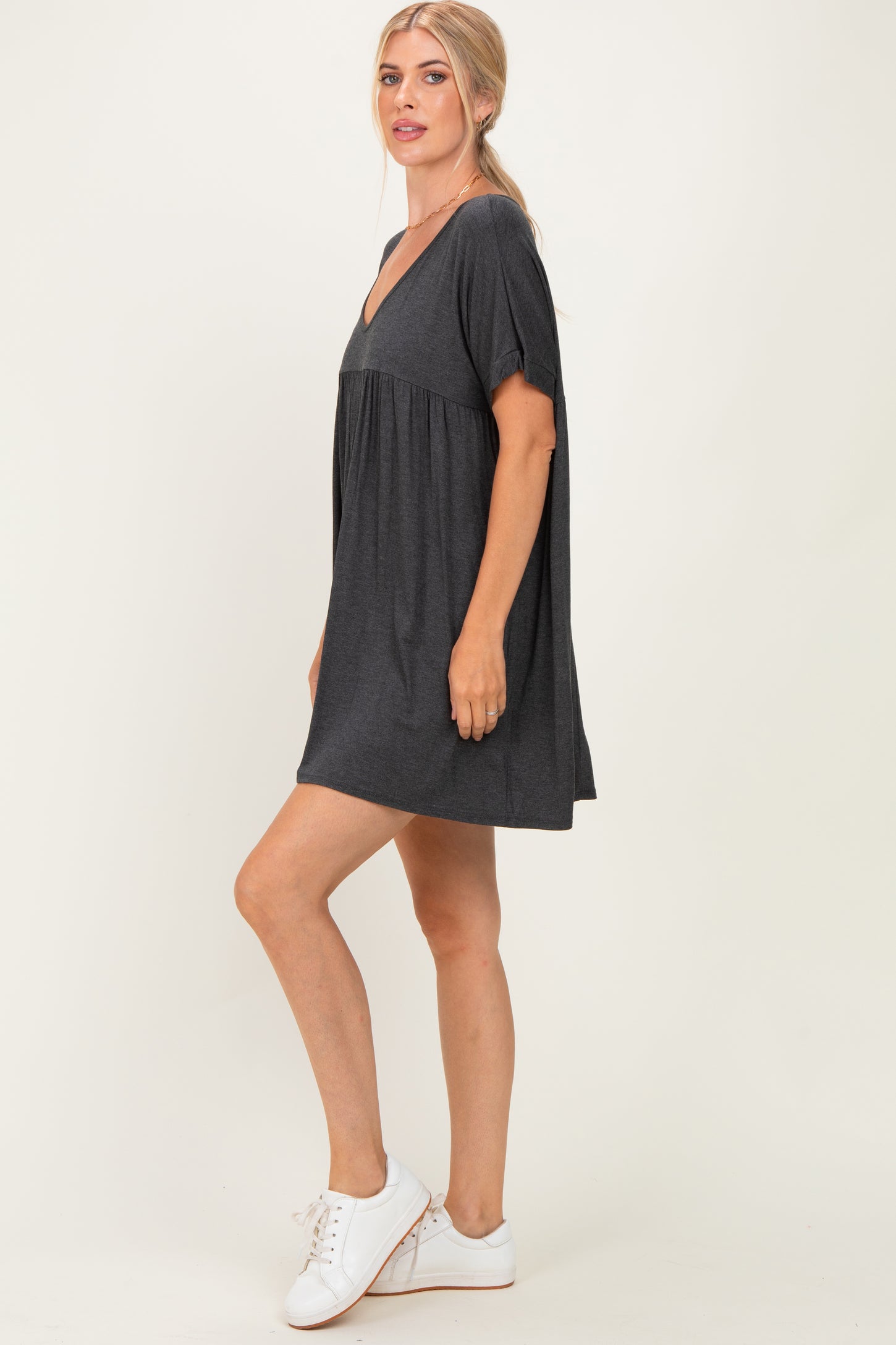 woman wearing a dark gray short sleeve v-neck dress with a flared hem and white sneakers