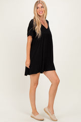 woman wearing a short black v-neck dress with short sleeves and a loose fit, standing against a plain background