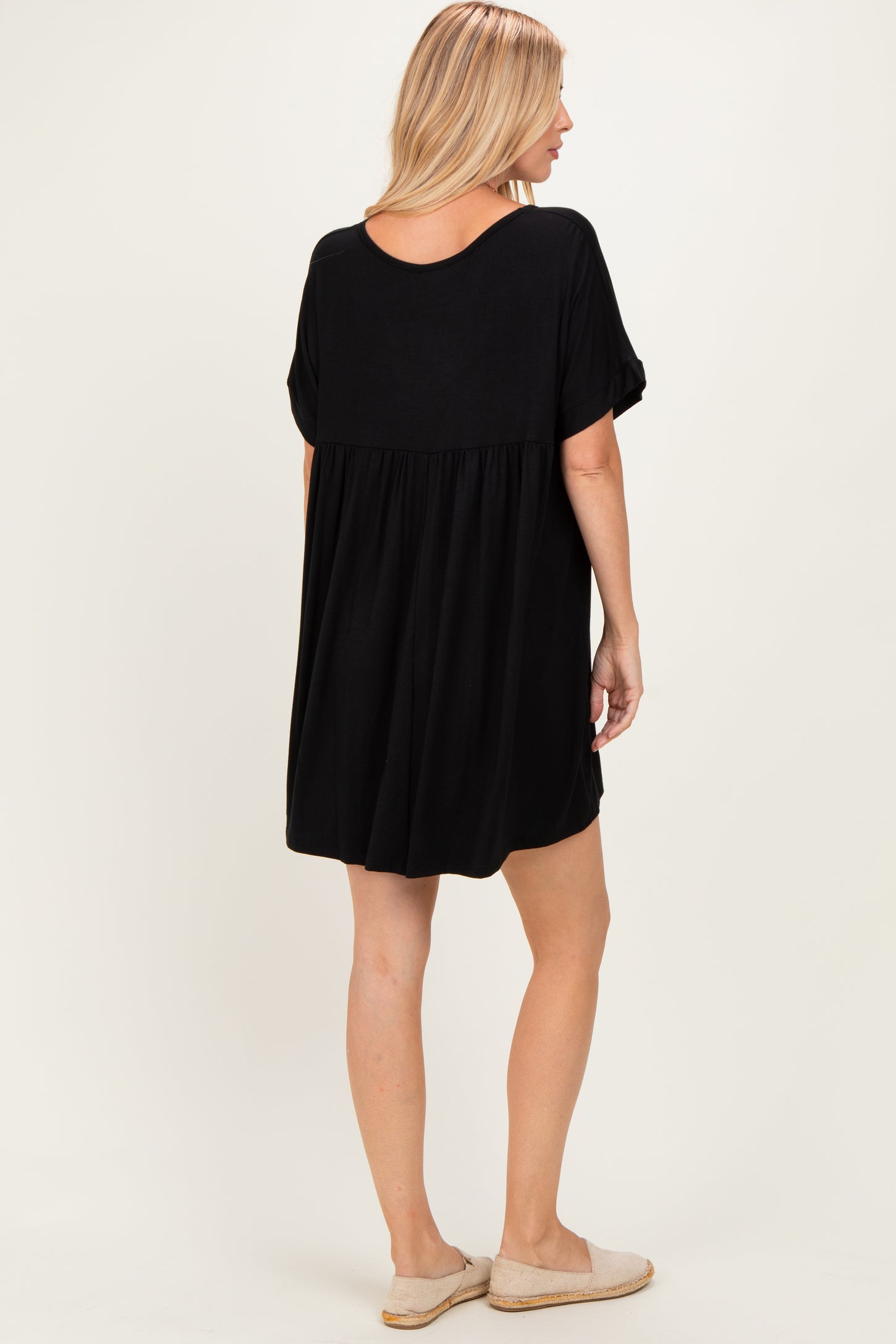 woman wearing a black short sleeve loose fit dress with a gathered back detail and casual slip-on shoes