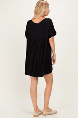 woman wearing a black short sleeve loose fit dress with a gathered back detail and casual slip-on shoes