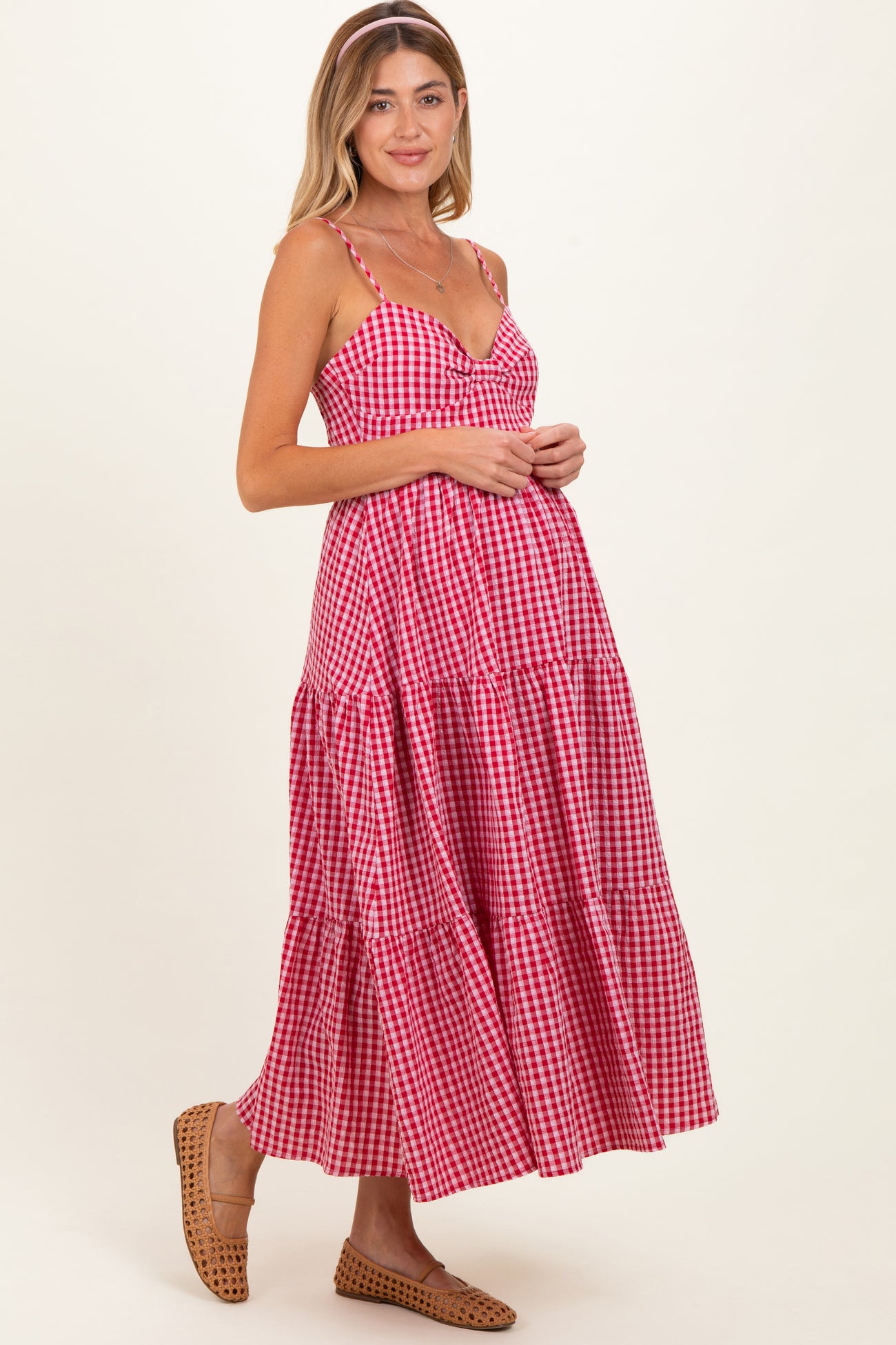 woman wearing a red and white gingham maternity dress with tiered skirt and spaghetti straps, showing her baby bump