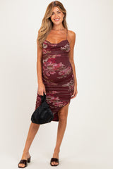 woman wearing a burgundy floral maternity dress with ruching and a thigh-high slit, holding a black bag and showing her baby bump