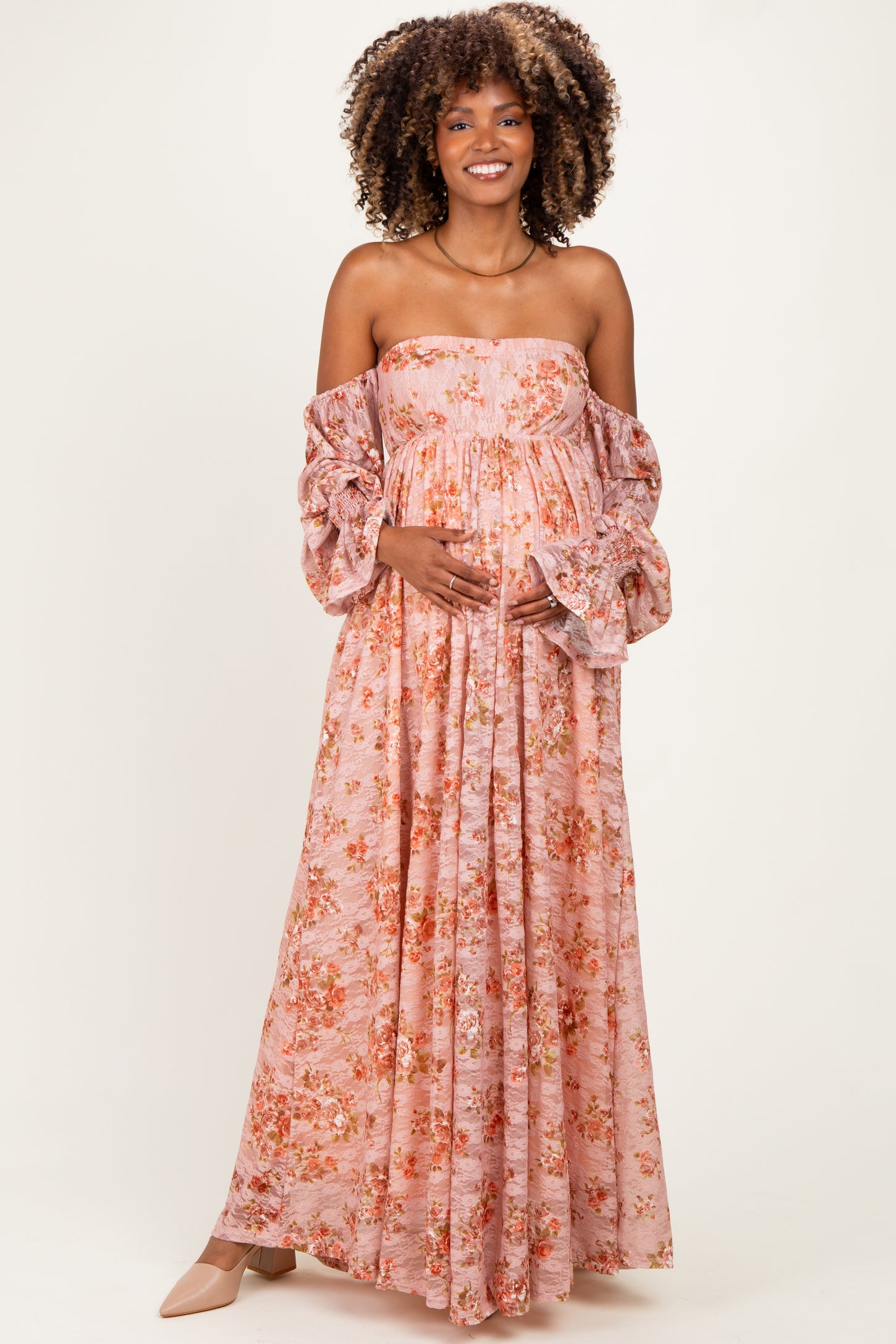 woman wearing a pink floral off-shoulder maternity gown with puff sleeves and crisscross detailing, holding her baby bump