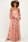 woman wearing a pink floral off-shoulder maternity gown with puff sleeves and crisscross detailing, holding her baby bump