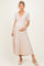woman wearing a light beige short sleeve maternity dress, holding her baby bump with a flowy skirt and espadrille shoes