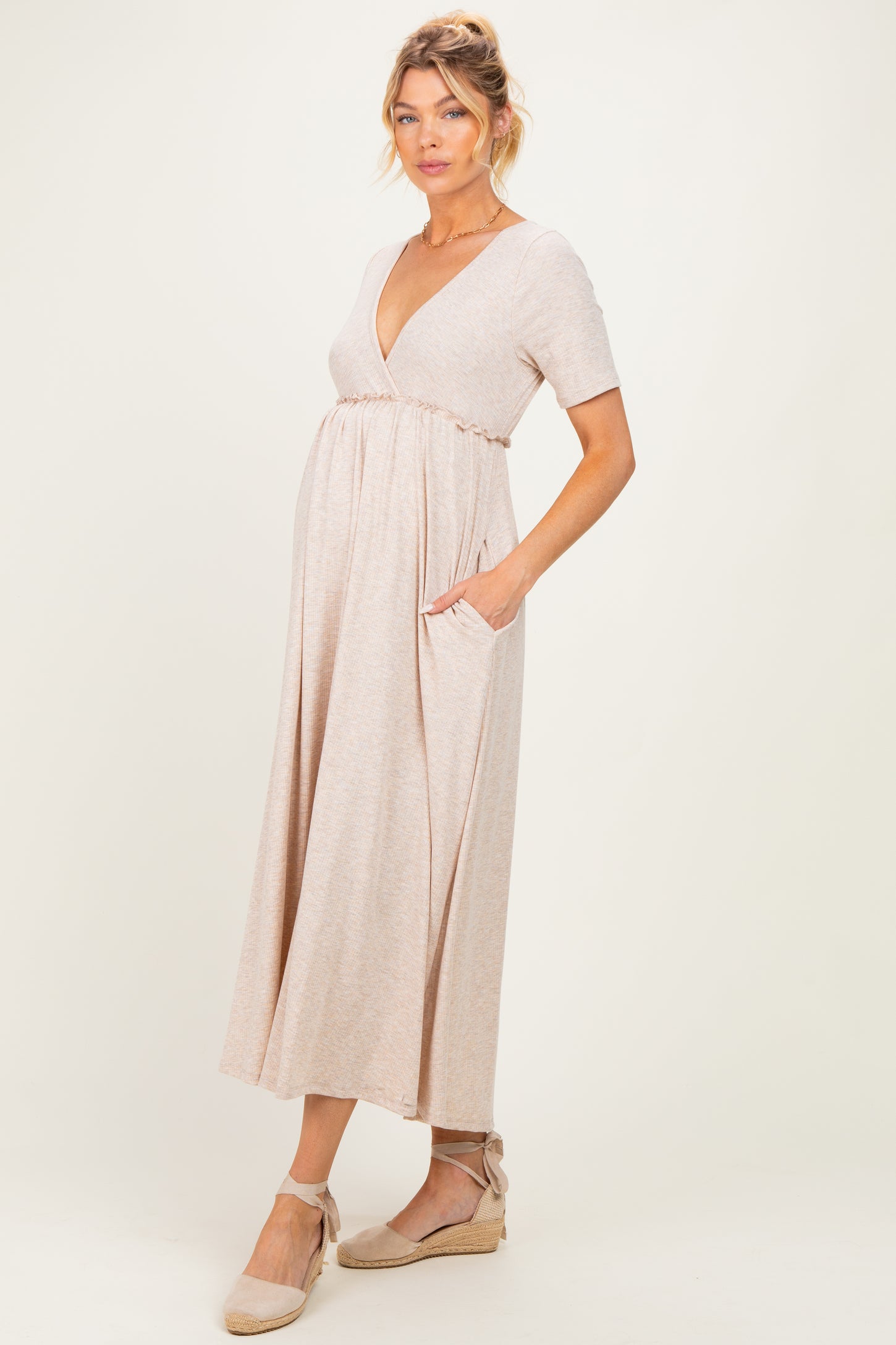 woman wearing a beige short sleeve maternity dress with a deep v-neckline and pockets, showcasing her baby bump