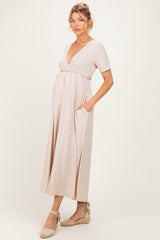 woman wearing a beige short sleeve maternity dress with a deep v-neckline and pockets, showcasing her baby bump