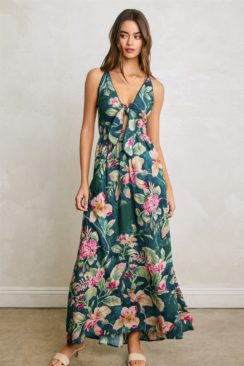 woman wearing a green floral maxi dress with a tie front and spaghetti straps, standing on a neutral background