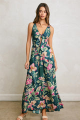 woman wearing a green floral maxi dress with a tie front and spaghetti straps, standing on a neutral background