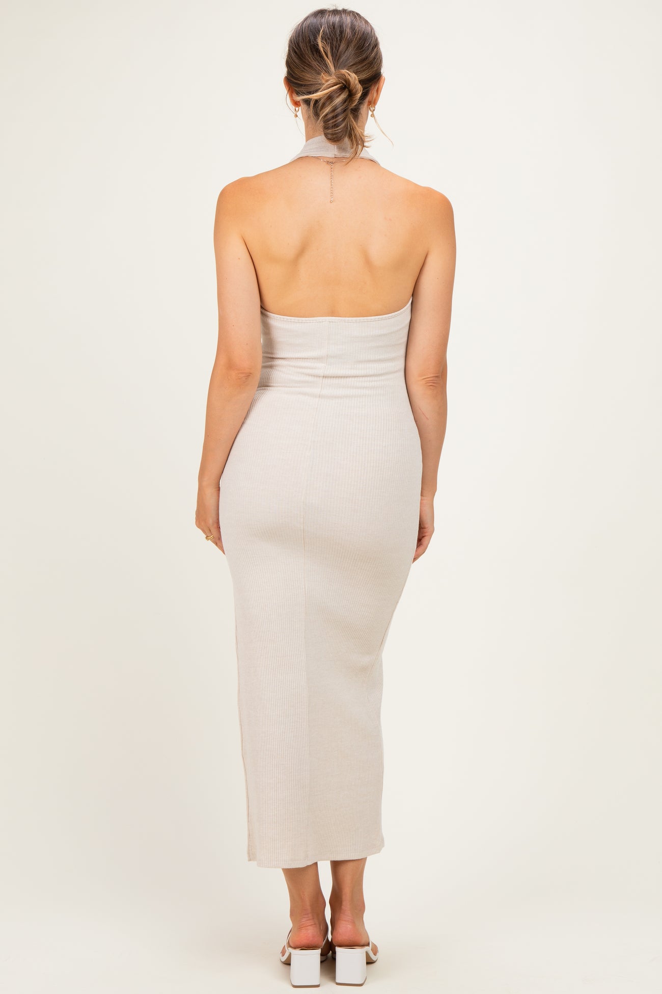 woman wearing a beige ribbed halter neck maternity dress, showing off her baby bump from the back