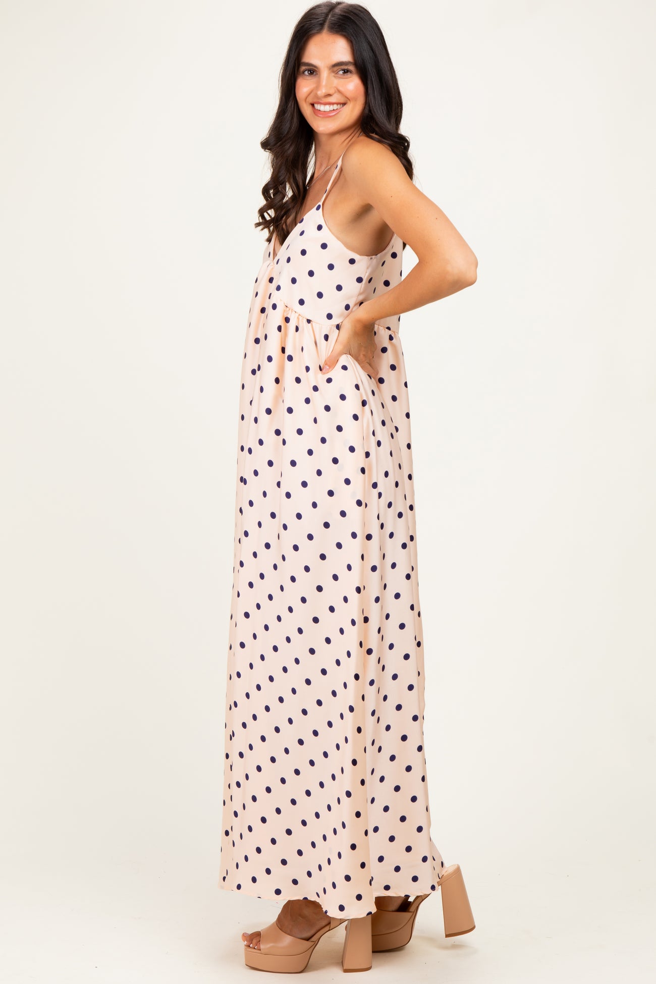 woman wearing a pink polka dot maxi dress with pockets and a flowy silhouette, standing sideways with a smile