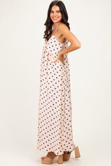 woman wearing a pink polka dot maxi dress with pockets and a flowy silhouette, standing sideways with a smile