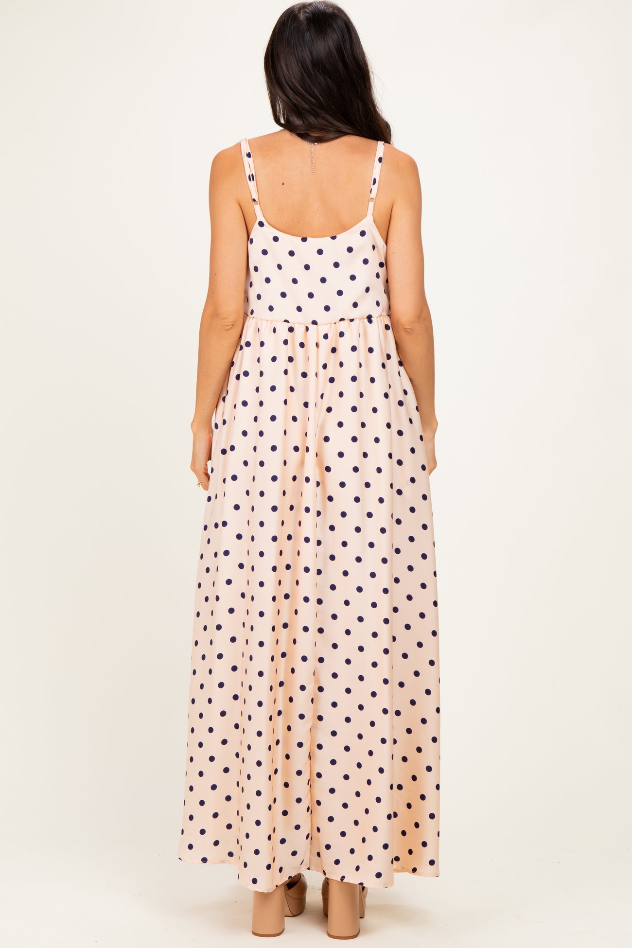 woman wearing a pink maxi dress with navy polka dots and adjustable straps, seen from the back