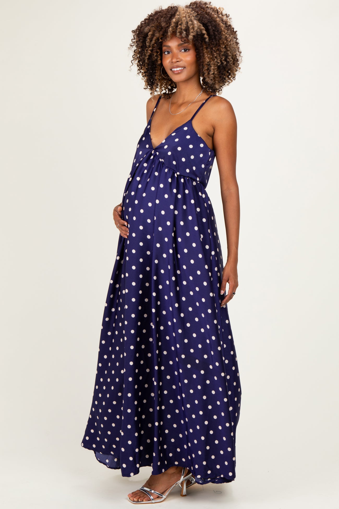woman wearing a navy blue polka dot maternity maxi dress and holding her baby bump