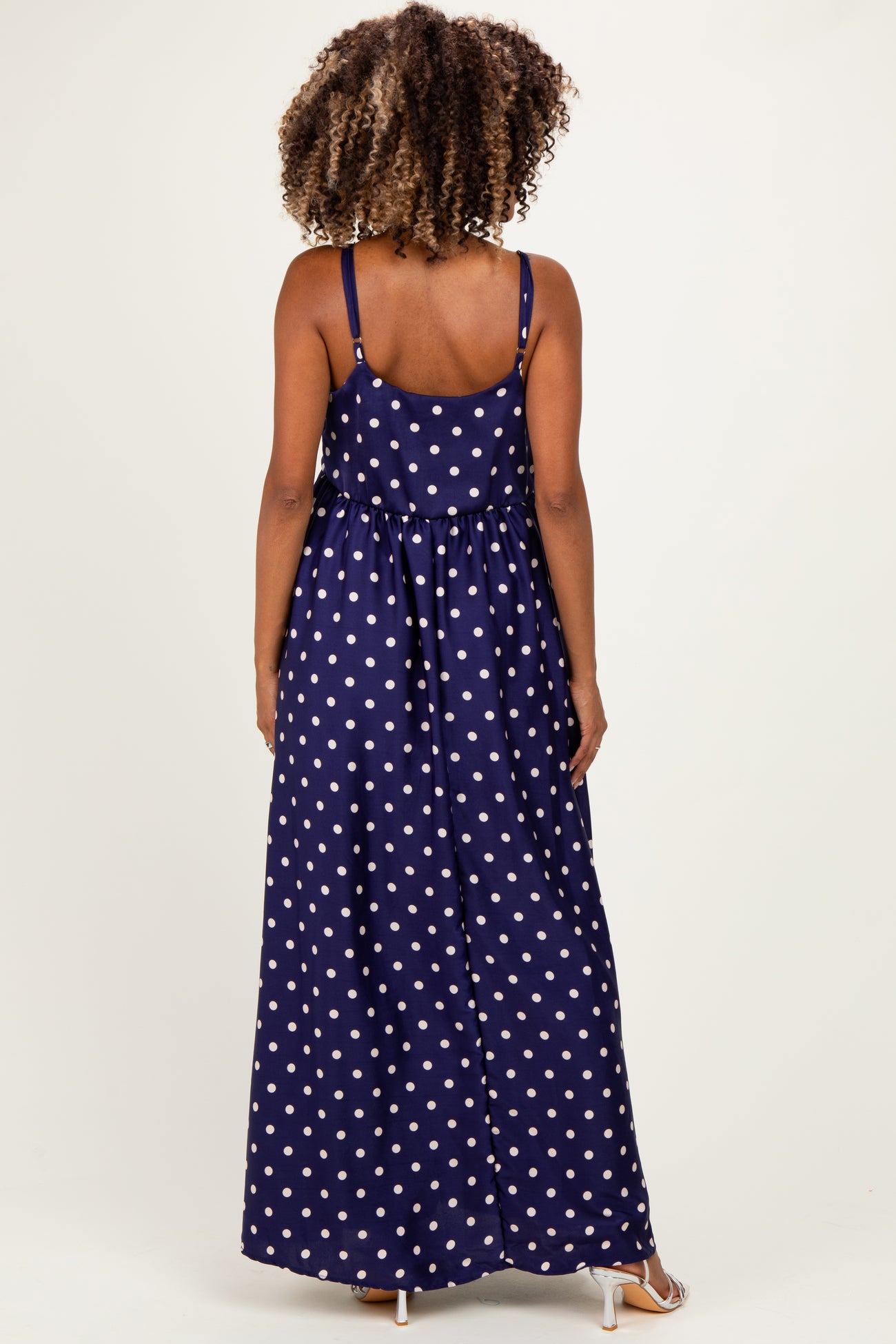 woman wearing a navy blue polka dot maxi maternity dress, showing the back view and adjustable straps