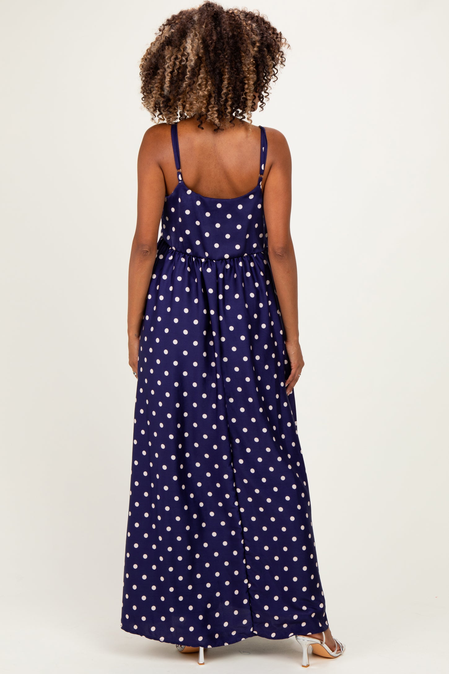 woman wearing a navy blue polka dot maxi maternity dress, showing the back view and adjustable straps