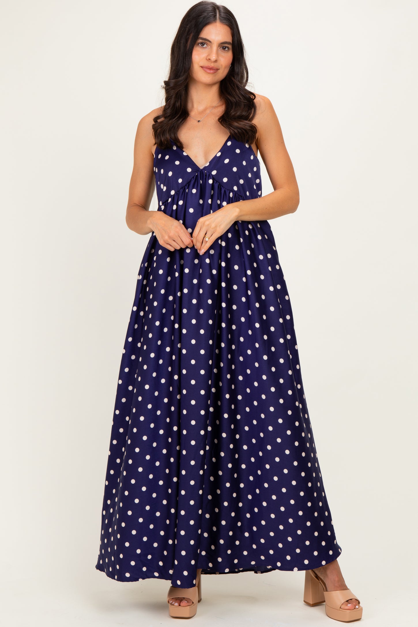 woman wearing a navy blue polka dot maxi dress with a tie detail at the bust and a flowing skirt