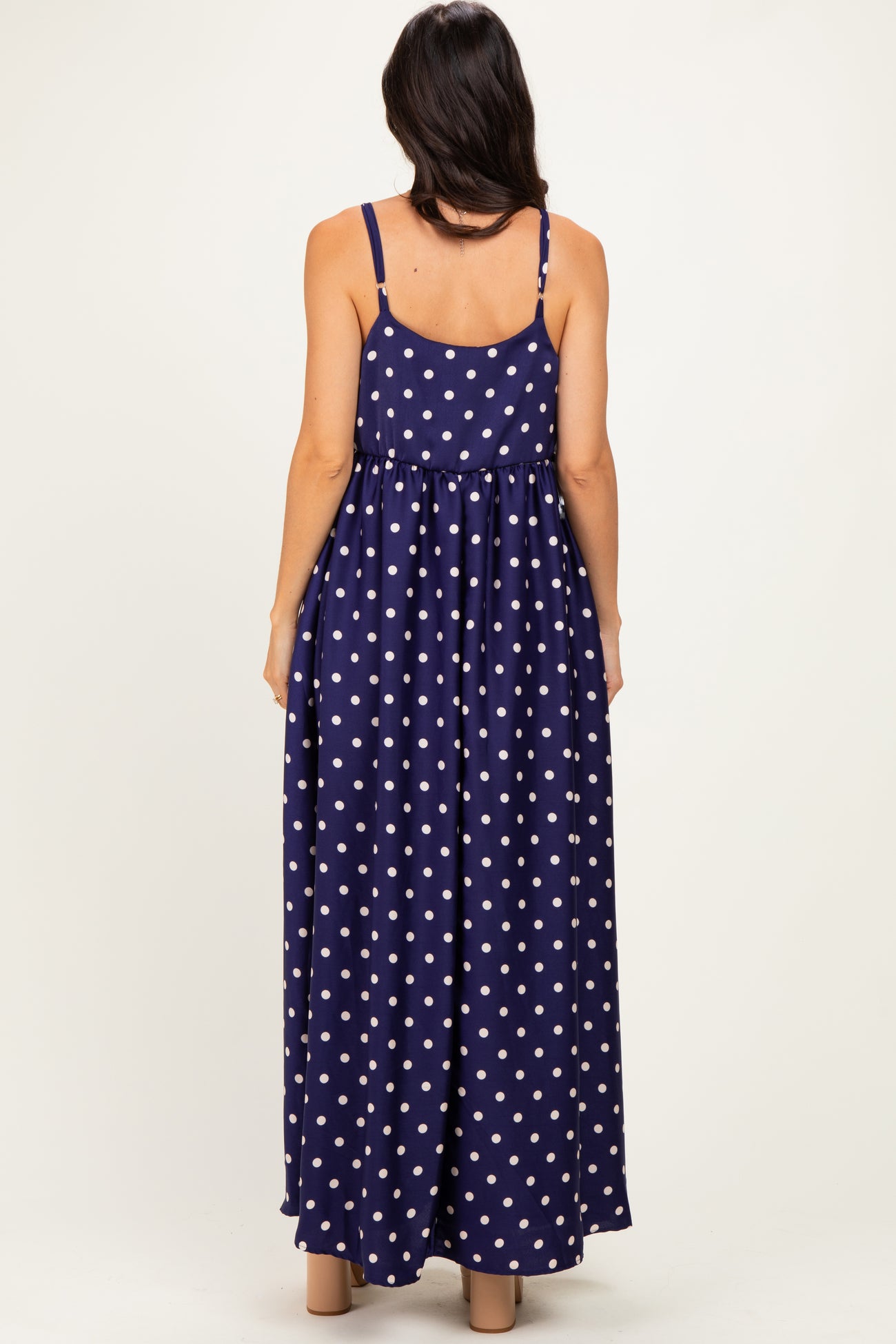 woman wearing a navy blue polka dot maxi dress with a flowy skirt and adjustable spaghetti straps from the back