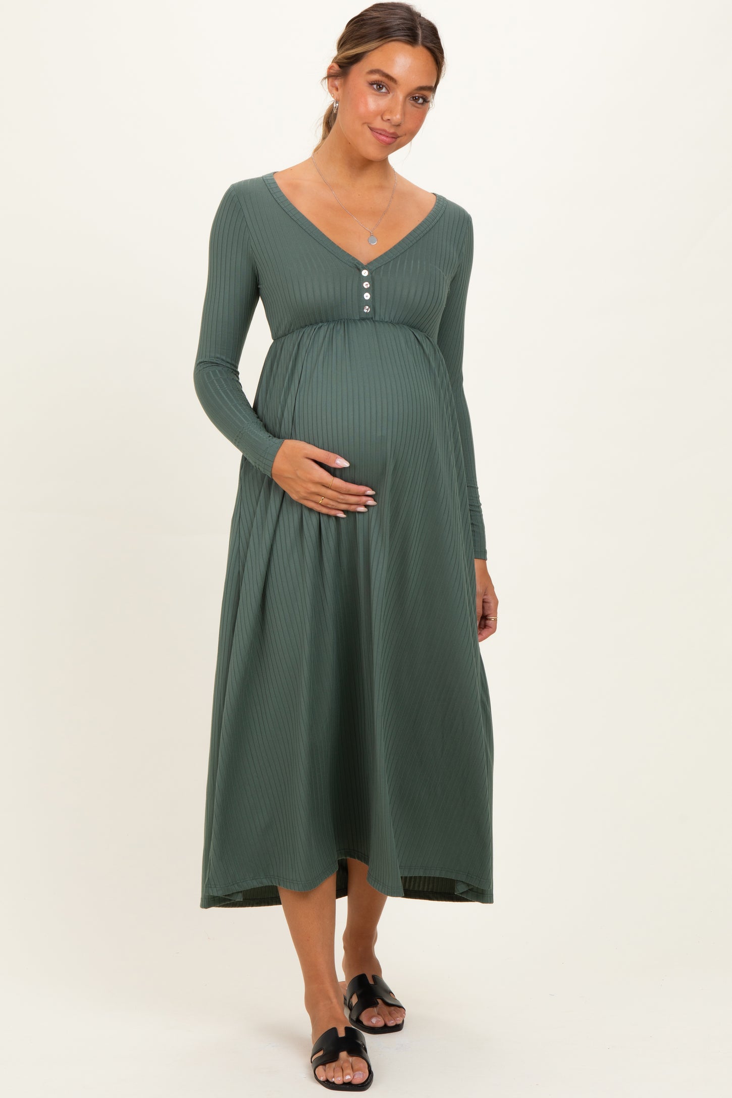 woman wearing a green ribbed maternity dress with long sleeves and button detail, holding her baby bump