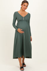 woman wearing a green ribbed maternity dress with long sleeves and button detail, holding her baby bump