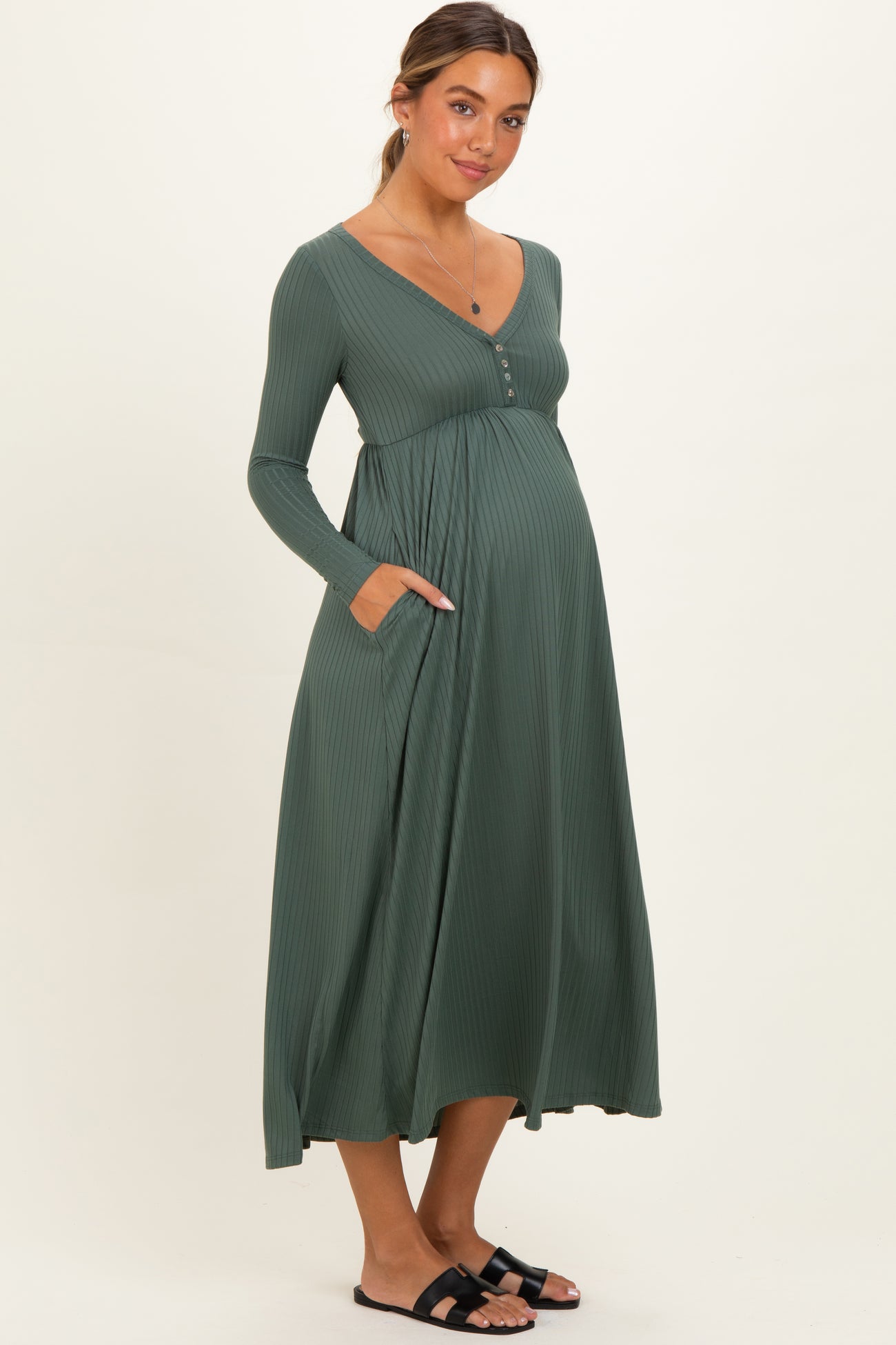 woman wearing a dark green long sleeve maternity dress with a button detail and pockets, showing her baby bump