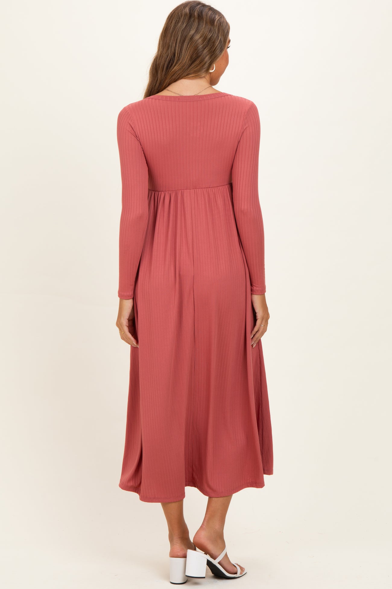 woman wearing a dusty rose long sleeve maternity dress with a flowing skirt and a fitted bodice, viewed from the back