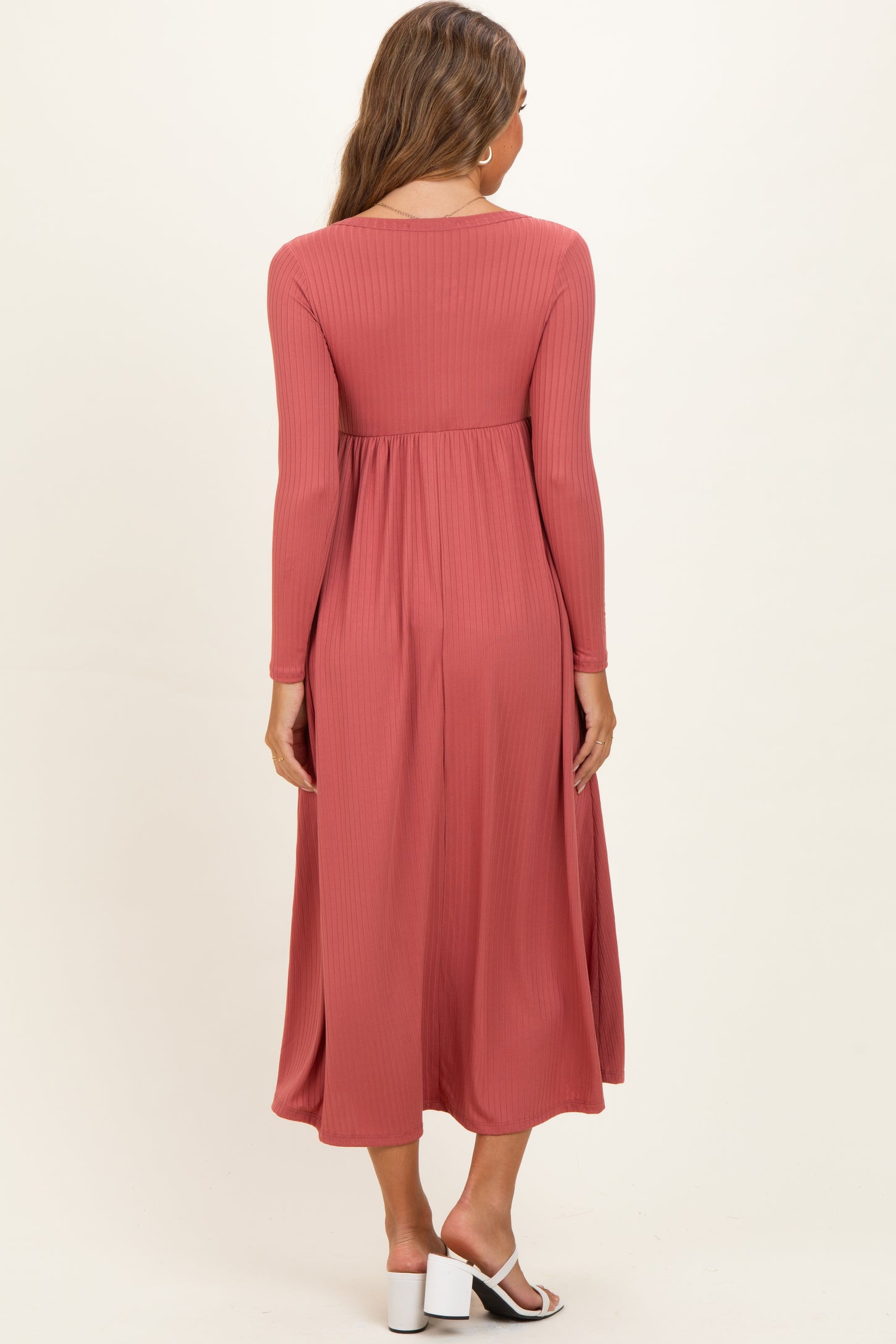 woman wearing a dusty rose long sleeve maternity dress with a flowing skirt and a fitted bodice, viewed from the back