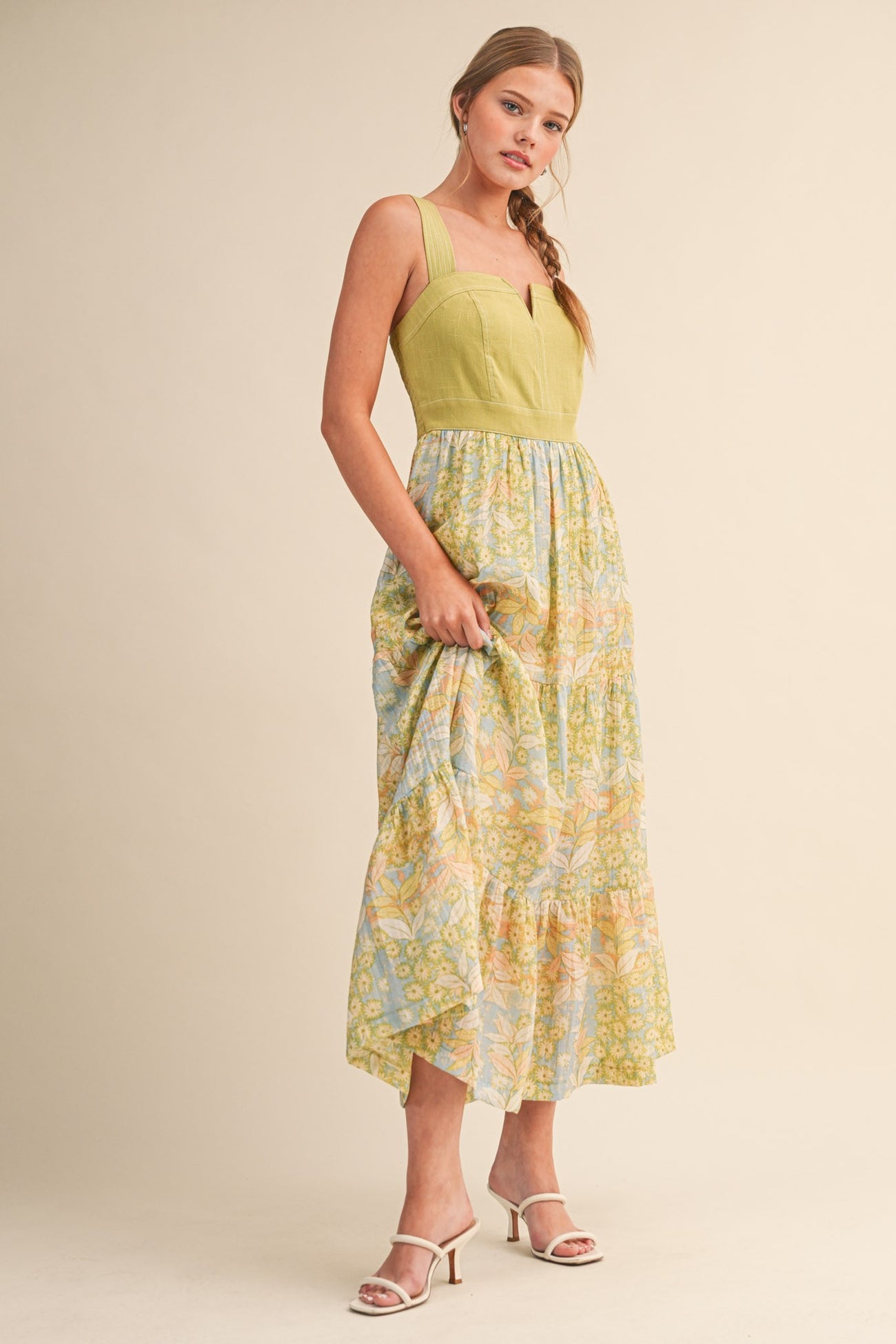 woman wearing a yellow and blue floral maxi dress with a fitted bodice and tiered skirt, standing with one hand on her hip