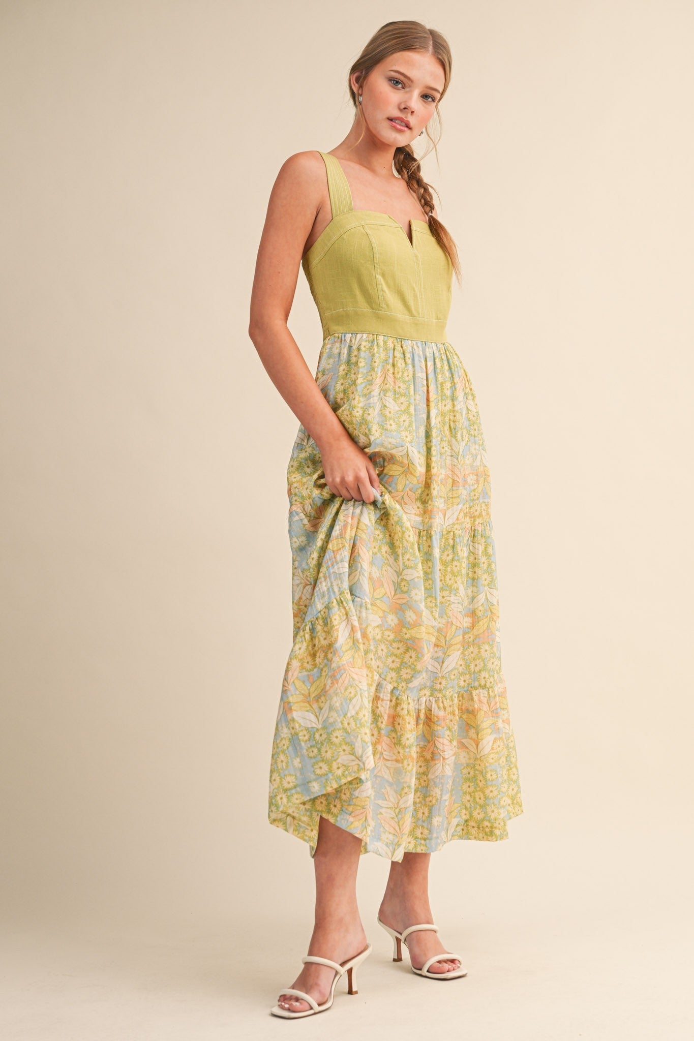 woman wearing a yellow and blue floral maxi dress with a fitted bodice and tiered skirt, standing with one hand on her hip