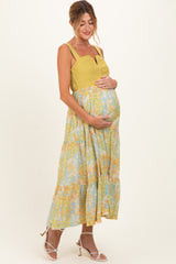 woman wearing a yellow maternity dress with a tiered floral skirt and holding her baby bump