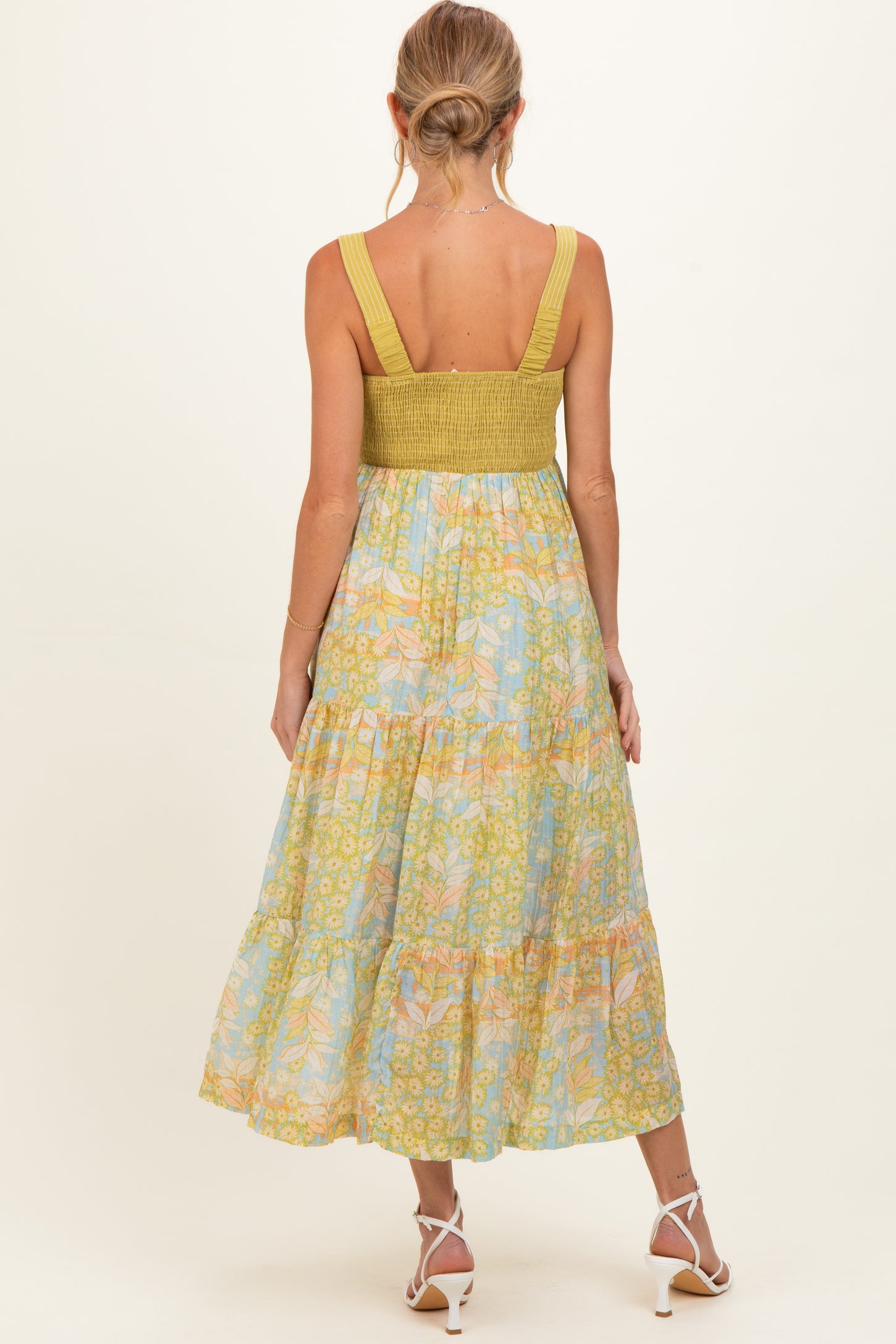 woman wearing a floral-patterned maternity dress with a smocked bodice and tiered skirt, showing a baby bump from the back