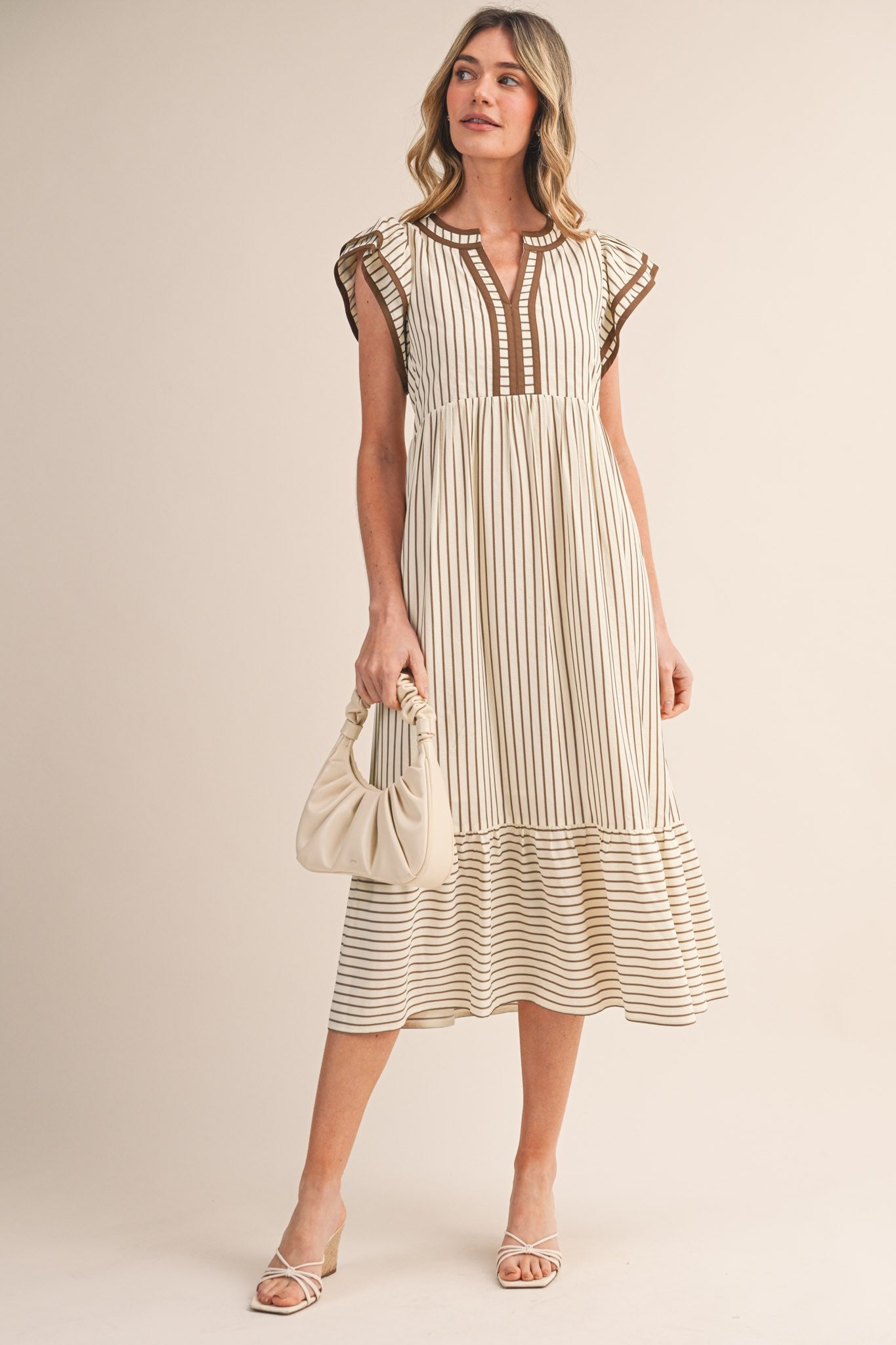 woman wearing a cream striped midi dress with cap sleeves and a ruffled hem, holding a beige purse